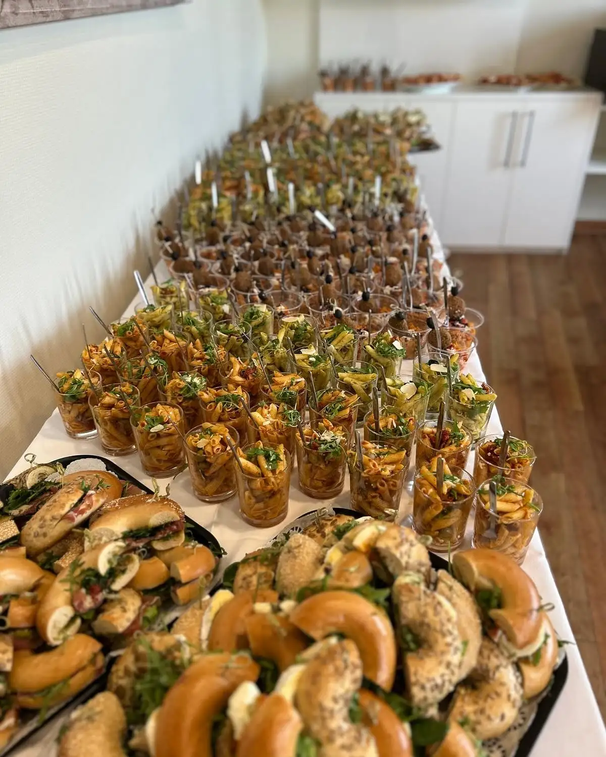 Lange Catering-Tafel mit Pastabechern in Gläsern und Platten mit belegten Bagels